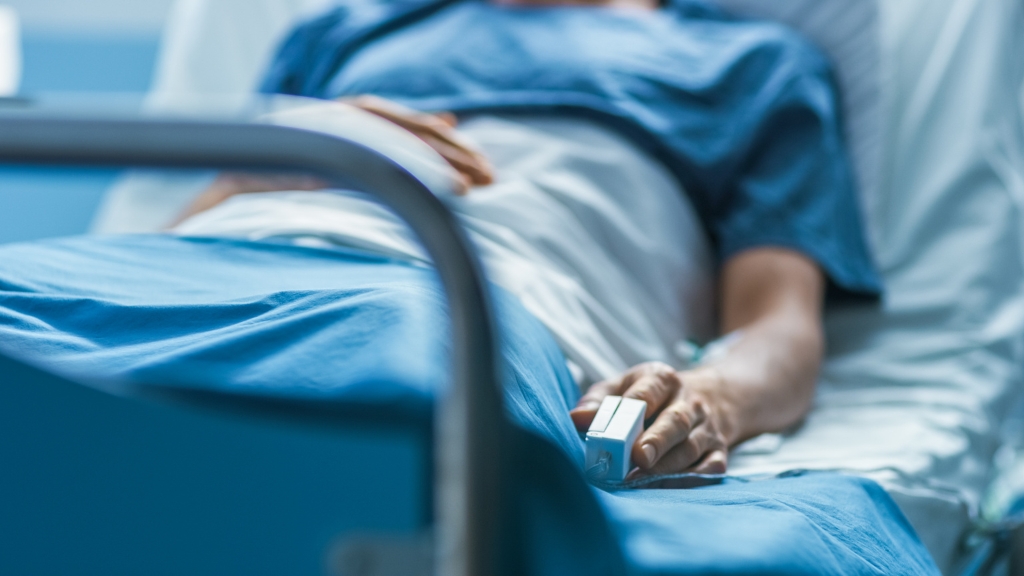 Person lying in a hospital bed with a pulse oximeter on their finger.