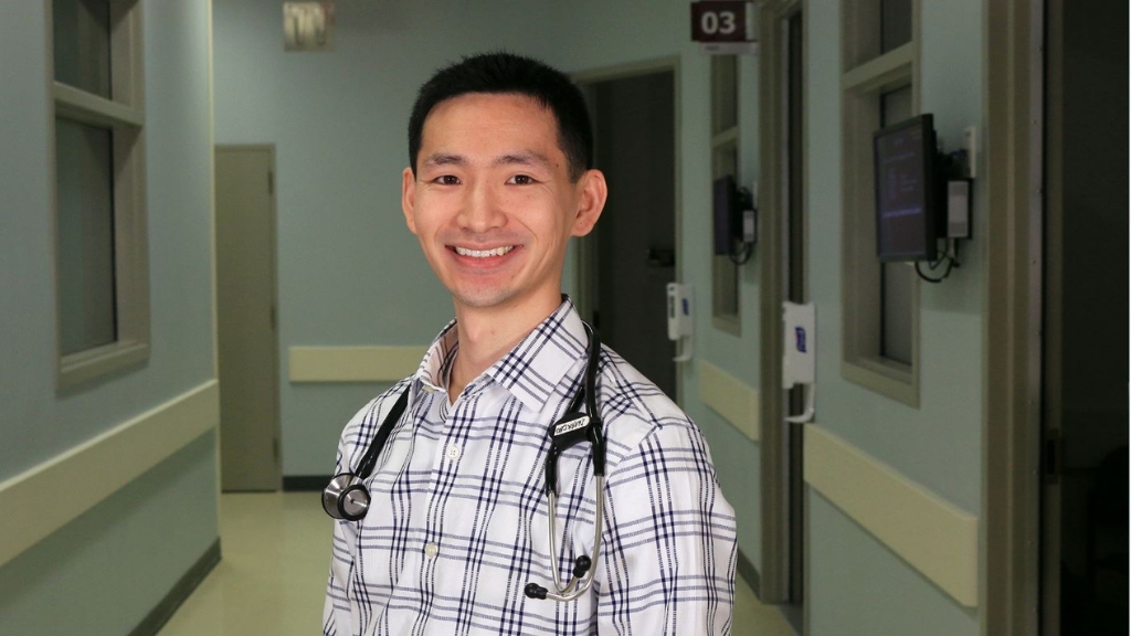 Derek Chu smiling for a photo in a hospital hallway.